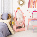 Pink crown-top dressing mirror with a storage shelf beside a bed.