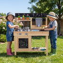Two children beside the Natural wooden mud kitchen in a garden with example play materials