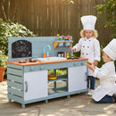 Children beside the Blue wooden mud kitchen outdoors with example play accessories and chef clothing