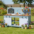 Blue wooden mud kitchen in a garden with example plants, cookware and toy food