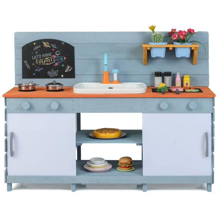 Blue wooden mud kitchen with sliding doors, sink and two flowerpots, staged with example cookware, toy food and plants