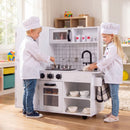 Children using the white and black play kitchen in a playroom; chef outfits and extra props are not included