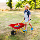 Red children’s wheelbarrow carrying example play accessories on grass