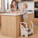 Child standing on the beige and grey step stool at a kitchen island with an adult nearby